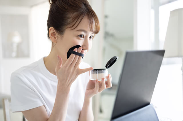 鏡を見ながらファンデーションを使う女性